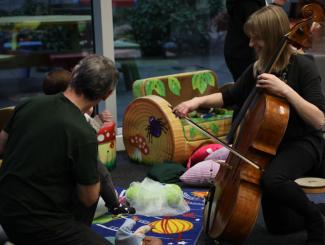 woman playing cello with father and child watching