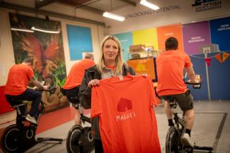 Woman standing in front of 3 men on exercise bikes