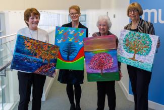 Four women standing with paintings