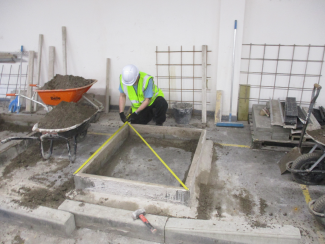 Man measuring concrete structure surrounded by various tools